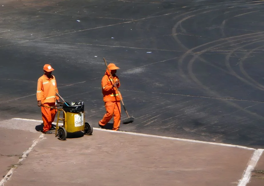 A professional cleaner in a red uniform holding a vacuum near a van, ready for service.